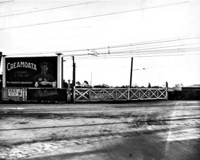 Moorabbin railway gates on Point Nepean Road. Advertisment for Creamota and Pelaco Shirts in background [picture].