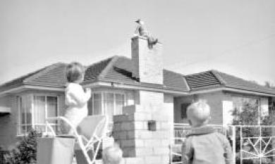 Father Christmas on the chimney of a house [picture].